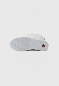 Vit gummi-sandal med en texturerad grå sula, med en röd detalj på remmen. Designen är minimalistisk och platt.