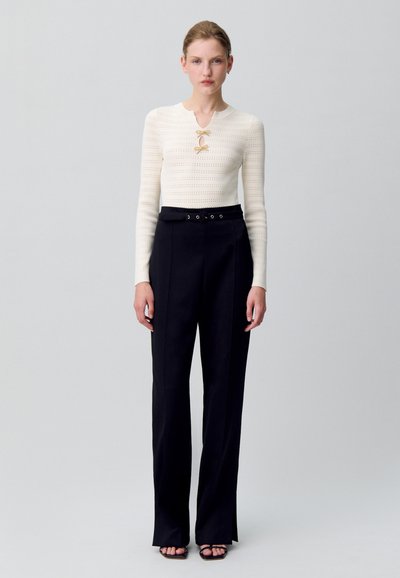 Top de punto blanco con escote redondo y un detalle de lazo, combinado con pantalones negros de talle alto que cuentan con una cintura ceñida y piernas anchas.