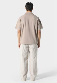 Koszula z krótkim rękawem w jasnobrązowym kolorze z fakturowanym wzorem, w połączeniu z luźnymi, jasnobeżowymi spodniami i białymi butami.