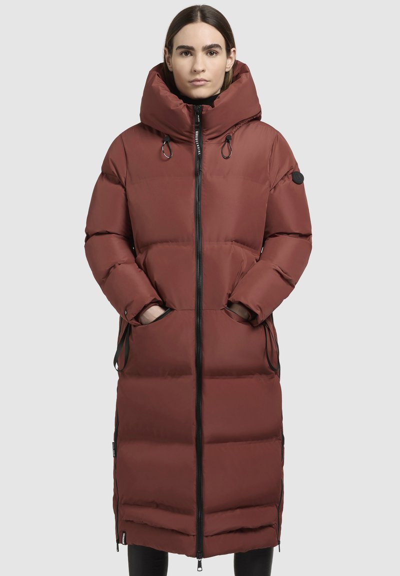 Röd vadderad lång jacka med hög krage, justerbar huva och sidofickor. Har en hel dragkedja och svarta detaljaccents.