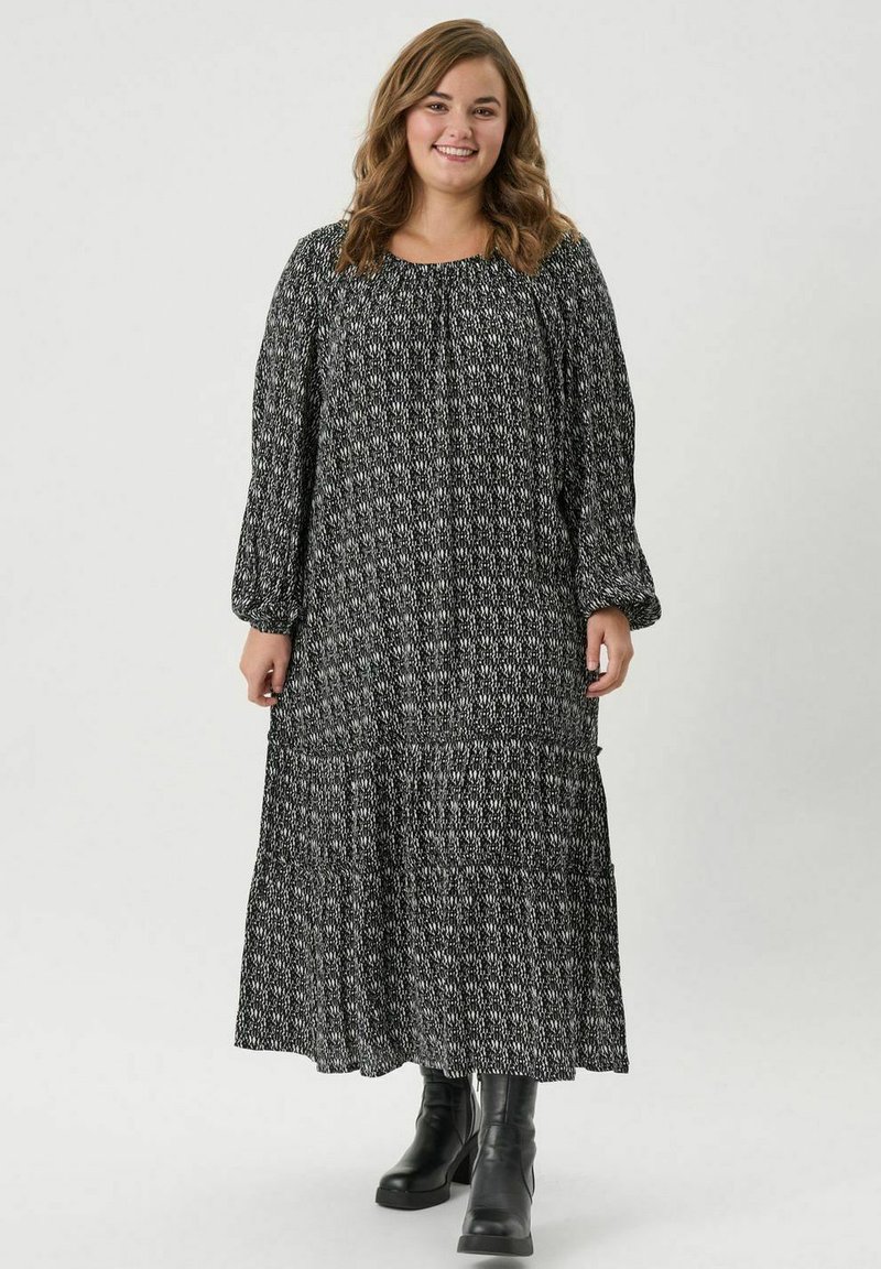 Vestido largo con estampado en blanco y negro, de mangas largas, con escote fruncido y diseño en capas. Se lleva con botas negras hasta la rodilla.