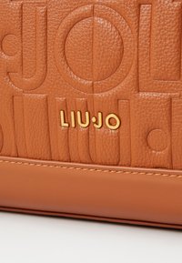 Bolso de cuero marrón con textura que presenta el logo grabado "LIUJO" y acentos de hardware dorado. Panel inferior liso con detalle de costura contrastante.
