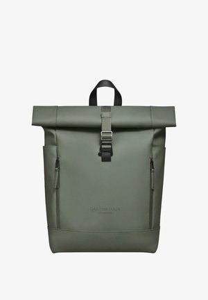 Olive spalvos medžiagos kuprinė su sukamos galvutės viršumi, turinti užtrauktuko kišenę, reguliuojamą diržą su metaline sagtimi ir priekinį logotipo aprašymą.