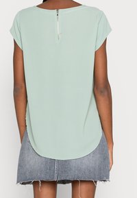 Haut vert menthe à manches courtes avec un ourlet arrondi et une fermeture éclair argentée au dos, associé à une jupe en denim effilochée.