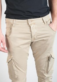 Beige cargobroek met een slim fit, voorzien van zakken met ritssluiting aan de zijkanten, gestikte details en contrasterende stofstructuur. Gemaakt van lichtgewicht materiaal.