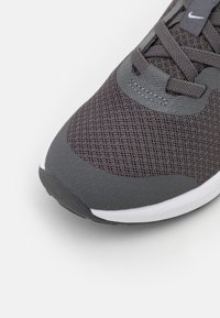 Ciemnoszary but sportowy z siateczkową cholewką i teksturowanymi akcentami. Posiada białą podeszwę środkową oraz przeszycia wokół sznurowadeł.