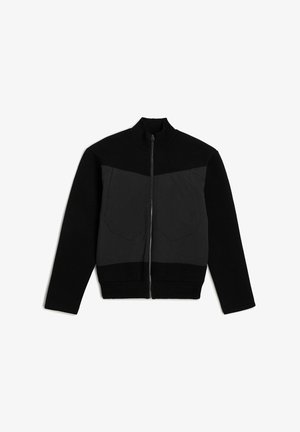 Giacca nera con zip, caratterizzata da un collo a maglia e una sezione frontale testurizzata con due taschini sul petto. Materiali a contrasto, vestibilità slim.