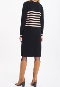 Svart stickad klänning med ett randigt beige mönster på ryggen, med sidoflikar och långa ärmar, matchad med knähöga beige stövlar.