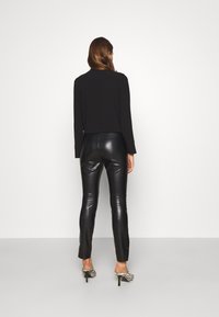 Top nero a maniche lunghe abbinato a pantaloni in pelle nera lucida con una vestibilità slim. La modella indossa scarpe con tacco con un motivo a strisce zebrate.