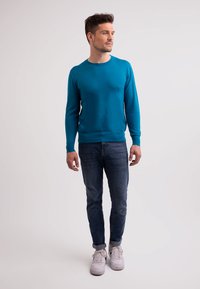 Teal crew-neck tröja i stickad tyg, figurnära siluett, kombinerad med slim-fit denim och vita sneakers, visad på manlig modell.