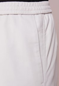 Lichtgrijze joggingbroek met een zachte textuur, elastische tailleband, zijzakken en geplooide ontwerpdetails.