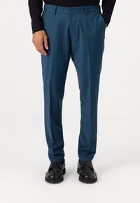 Pantalon de costume bleu canard avec un motif texturé, coupe droite, passants de ceinture et fermeture à bouton sur le devant. Porté avec des chaussures noires.