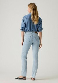 Jeans de tiro alto de color azul claro con un corte ajustado, combinados con una camisa de mezclilla y zapatos de tacón abierto negros. La tela parece suave y casual.