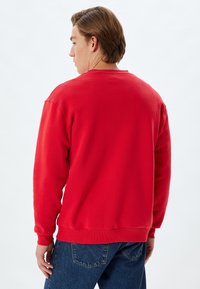 Sudadera roja con cuello redondo y puños acanalados, hecha de una tela suave. La vista trasera muestra un diseño sencillo sin patrones ni acentos adicionales.
