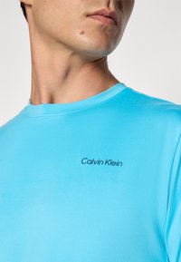 Hellblaues Baumwoll-T-Shirt mit Rundhalsausschnitt und kurzen Ärmeln, mit einem schwarzen "Calvin Klein"-Logo auf der linken Brustseite.