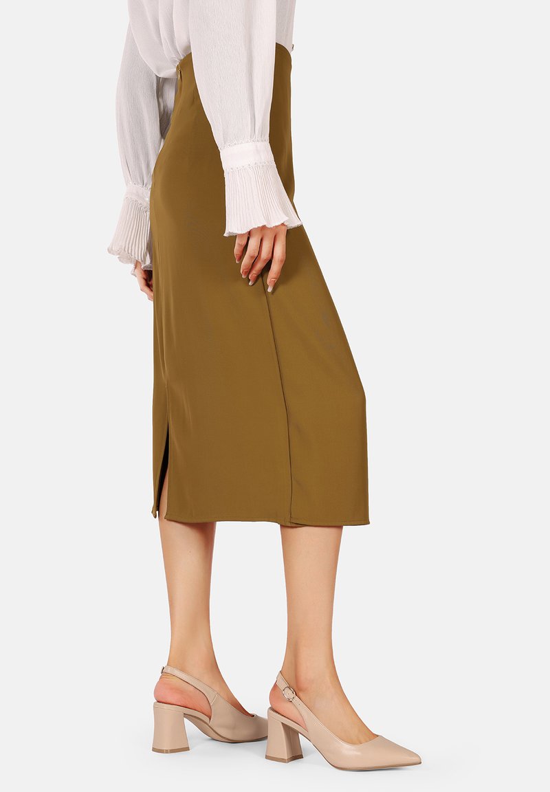 Falda midi verde oliva con abertura lateral, complementada con una blusa blanca texturada. Zapatos slingback de tacón bloque beige.