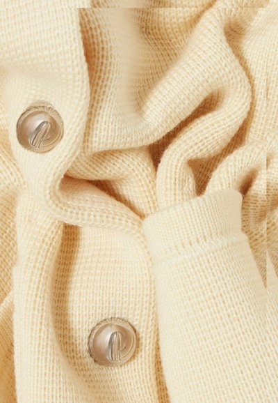 Tessuto di maglione beige lavorato a maglia, con una texture liscia e costine visibili, bottone argentato dettagliato con logo e design arricciato.