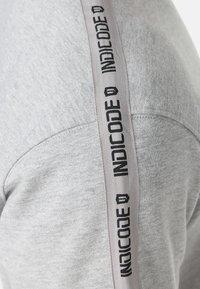 Gray sweatshirt featuring a soft texture, with a contrasting vertical striped design on the shoulder displaying "INDICODE" in black text.