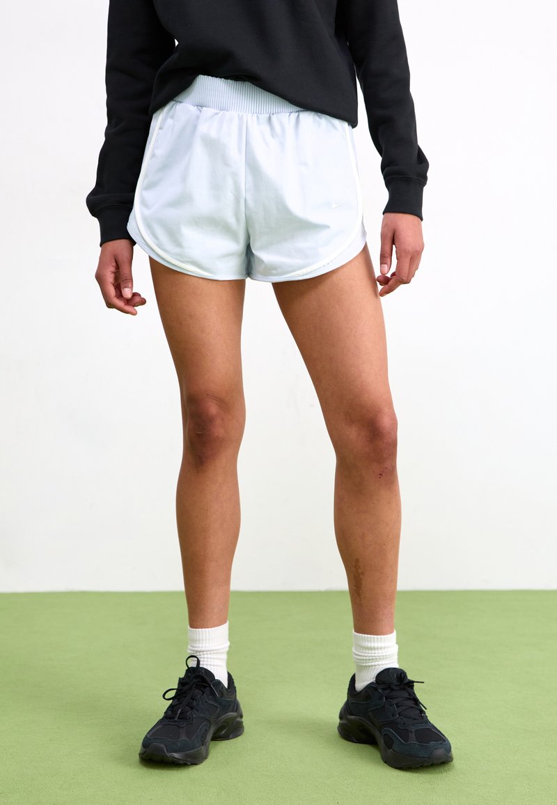 Šviesiai mėlyni sportiniai šortai su elastingu juosmeniu, kontrastinėmis baltomis detalėmis ir Nike logotipu; derinami su juodais sportbačiais ir baltais ilgaauliais šortais.