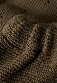 Tissu marron tricoté avec des mailles épaisses et texturées, présenté en gros plan avec des plis et un éclairage doux.