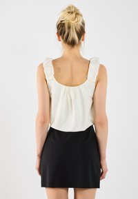 Hvit topp med volanger, kombinert med et tettsittende svart skjørt. Glatt tekstur, enkelt design, og kontrast mellom lyse og mørke farger.
