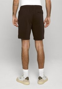 Bruine katoenen short met een elastische tailleband, zijzakken en een achterzak. Draagt witte sokken en sneakers. Gestructureerde pasvorm.