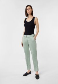 Czarny top bez rękawów, jasnozielone dopasowane spodnie z podwiniętymi mankietami oraz czarne mokasyny. Skupienie na wyraźnych liniach i gładkich fakturach.