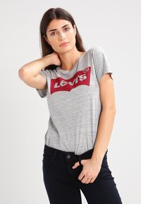 Grå T-shirt med korte ærmer, der har et fremtrædende rødt Levi's-logo på fronten. Stoffet ser blødt ud med en let meleret tekstur.