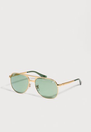 Lunettes de soleil aviateur dorées, aux verres vert pâle et aux embouts de branches vert foncé, sur un fond clair uni.