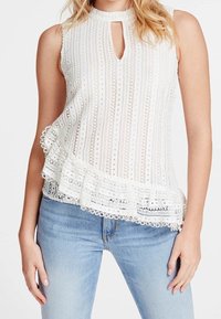 Top sin mangas blanco con escote en forma de llave, que presenta detalles de encaje, rayas verticales y un dobladillo con volantes y borde ondulado.