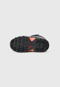 Semelle en caoutchouc noir avec une texture antidérapante, dotée d'une accent orange vif près du talon et d'une structure de talon renforcée pour le soutien.