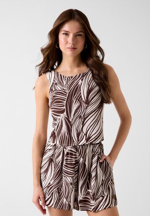 Giovane donna con lunghi capelli castani che indossa una canotta senza maniche con motivo astratto a foglie marroni e bianche e pantaloncini abbinati.