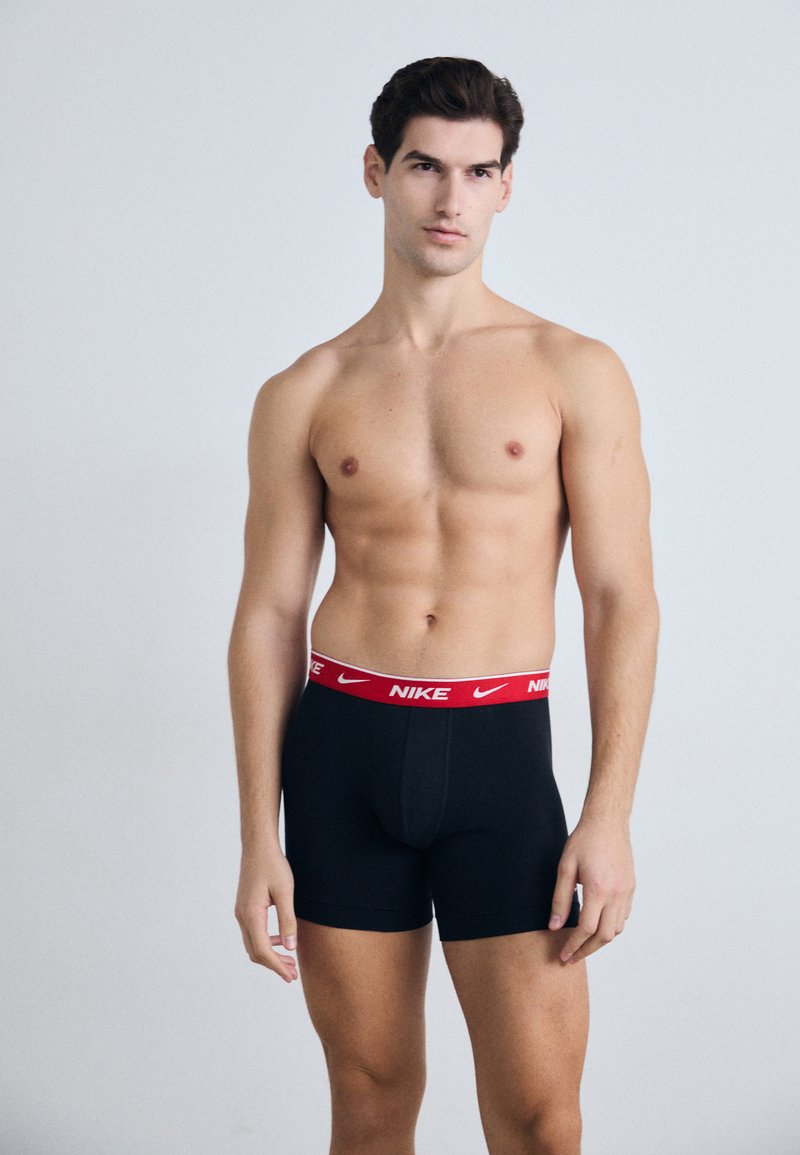 Fekete boxer alsónadrág, piros NIKE logós derékszorítóval. Az anyag rugalmasnak és simának tűnik. A modellen nincs felső, így jól látható a fazonja.