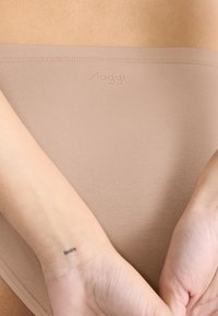 Nude naadloze bikini slipjes van zachte stof, met een bredere elastische tailleband met discrete branding en een gladde textuur.
