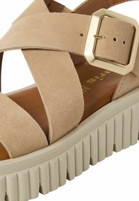 Beżowe zamszowe sandały z szerokim krzyżowym paskiem, złotym zapięciem oraz teksturowaną podeszwą platformową z żłobieniami.