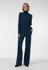 Ensemble en tricot deux pièces en teal profond, comprenant un haut à col montant à manches longues et un pantalon à jambes larges, avec une texture douce et une coupe décontractée.