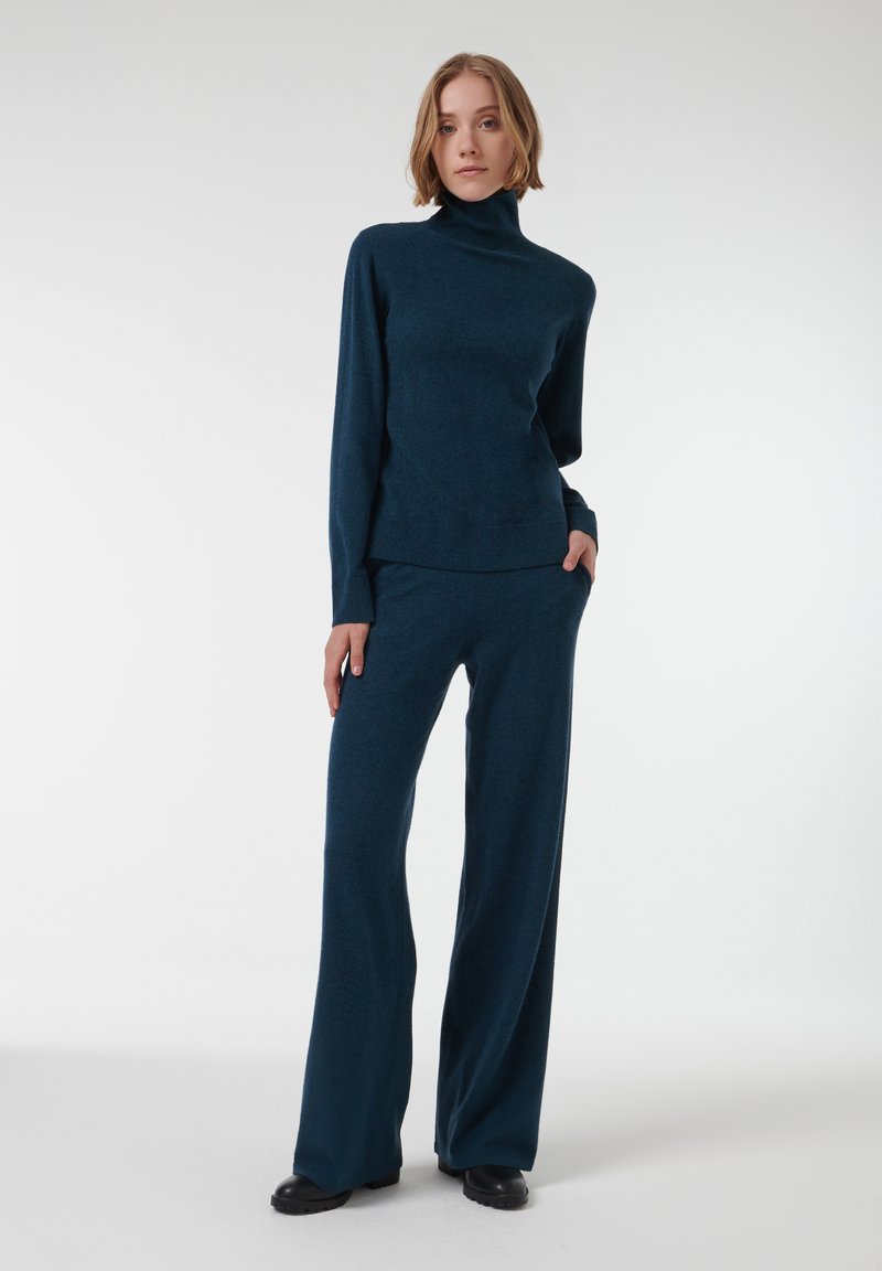 Ensemble en tricot deux pièces en teal profond, comprenant un haut à col montant à manches longues et un pantalon à jambes larges, avec une texture douce et une coupe décontractée.