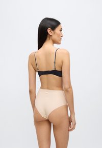 Μαύρο σουτιέν με ρυθμιζόμενους ιμάντες και κλείσιμο με αγκράφα, συνδυασμένο με μπεζ εσώρουχο ψηλόμεσο, με λεία υφή, μινιμαλιστικό σχέδιο, από πίσω πλευρά.