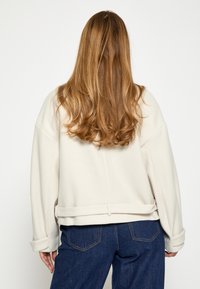 Sudadera de color crema, de corte amplio, con dobladillo curvado y puños enrollados, hecha de una tela suave. Combinada con unos jeans azul oscuro.