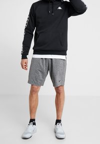 Sudadera negra con capucha, logo blanco y mangas a rayas, combinada con pantalones cortos grises y zapatillas deportivas blancas. Diseño simple y casual.