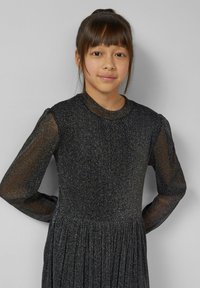 Zwarte jurk met lange, doorschijnende mouwen, gestructureerde stof met subtiele glans, ronde halslijn en een taille die is aangezet voor een uitlopende rok.