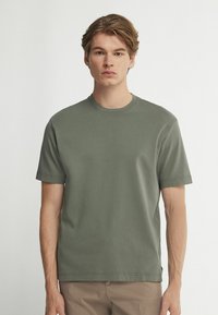 Olivgrön bomulls-t-shirt med rund hals, korta ärmar och avslappnad passform, med minimala sömmar och en etikett vid nederkant.