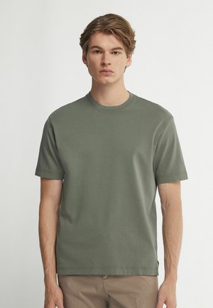 Olivgrünes Baumwoll-T-Shirt mit Rundhalsausschnitt, kurzen Ärmeln und lockerem Schnitt, das minimale Nähte und ein Etikett am Saum aufweist.