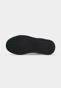 Semelle de chaussure noire avec motif antidérapant texturé et zone rectangulaire pour logo au centre sur fond gris clair uni.