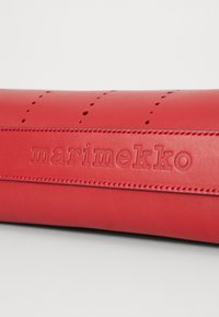 Röd läder pennfodral med präglad "marimekko" logotyp, med stygna detaljer och små perforeringar längs den övre kanten.