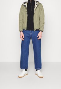 Chaqueta bomber verde oliva con forro de estampado floral, cuello de tortuga negro, vaqueros anchos de mezclilla azul y zapatillas blancas con suelas de goma.