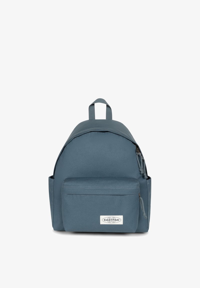 Zaino in tessuto blu con forma arrotondata, tasca frontale con zip, manico superiore e patch con logo sulla parte bassa anteriore. Materiale resistente.