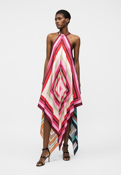 Γυναίκα που φοράει πολύχρωμο, γεωμετρικό φόρεμα με λουρί στο λαιμό και τελείωμα μαντηλιού, με κάθετες ρίγες σε κόκκινο, ροζ, άσπρο, πράσινο και πολύχρωμο, συνδυασμένο με μαύρες γόβες.