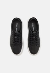 Czarne sneakersy z gładkim skórzanym noskiem, teksturowanymi bocznymi panelami, czarnymi sznurówkami i białymi gumowymi podeszwami. Na wkładce znajduje się logo Calvin Klein.