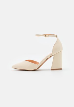 Beige high-heeled pump met een spitse neus, enkelbandje en een chunky hak. Gladde materialen en minimalistisch ontwerp.